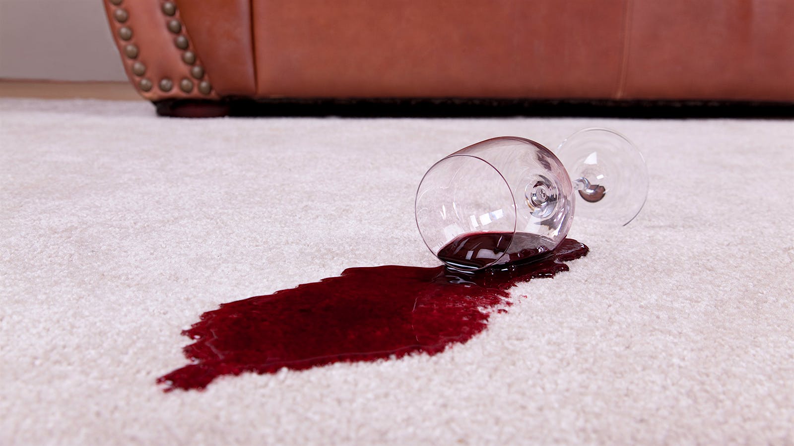 A glass of red wine spilling onto a carpeted floor